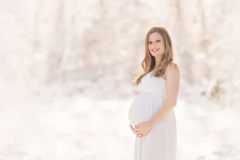 A pregnant woman in the snow posing for her maternity photoshoot