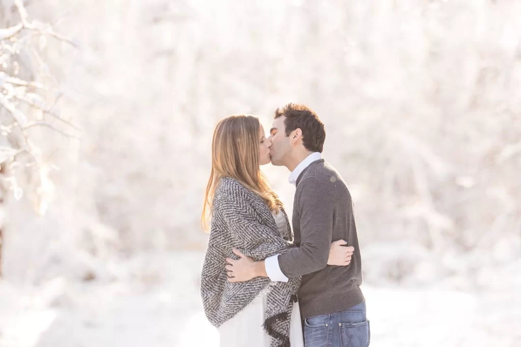 A pregnant woman and her husband in the snow posing together for their maternity photoshoot