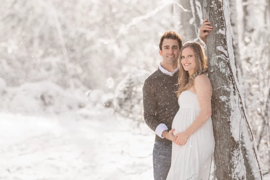 A pregnant woman and her husband in the snow posing together for their maternity photoshoot