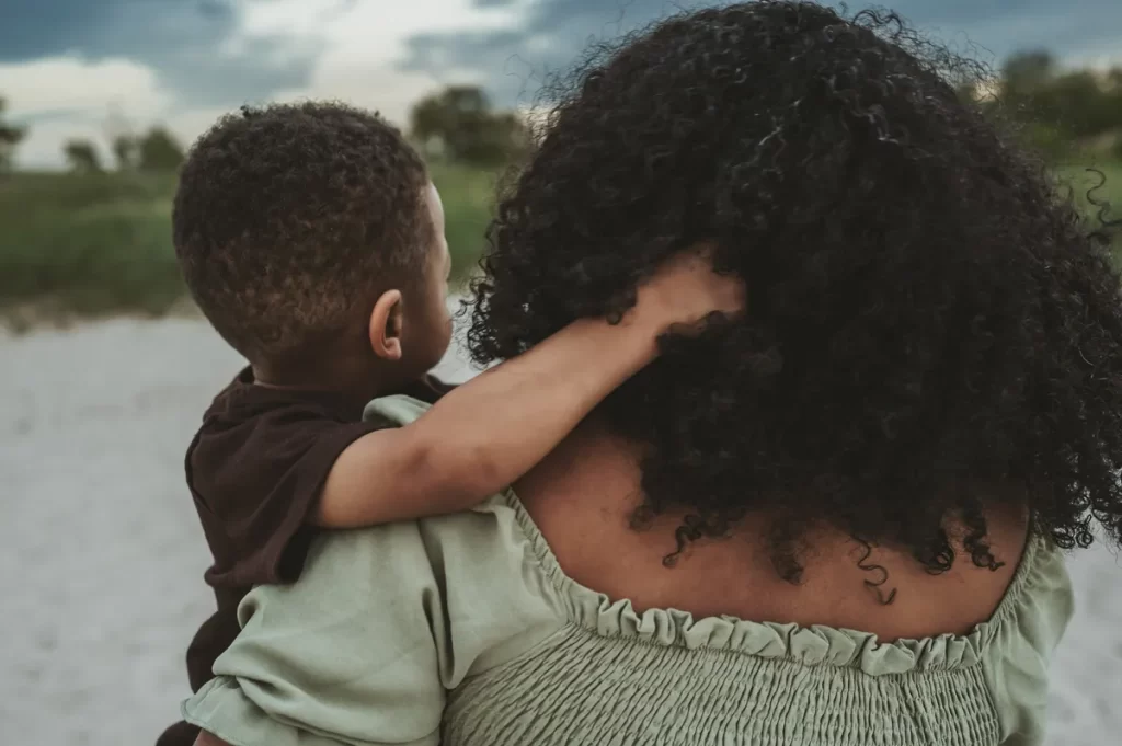 A little boy playing with his mom's curly hair as she holds him close