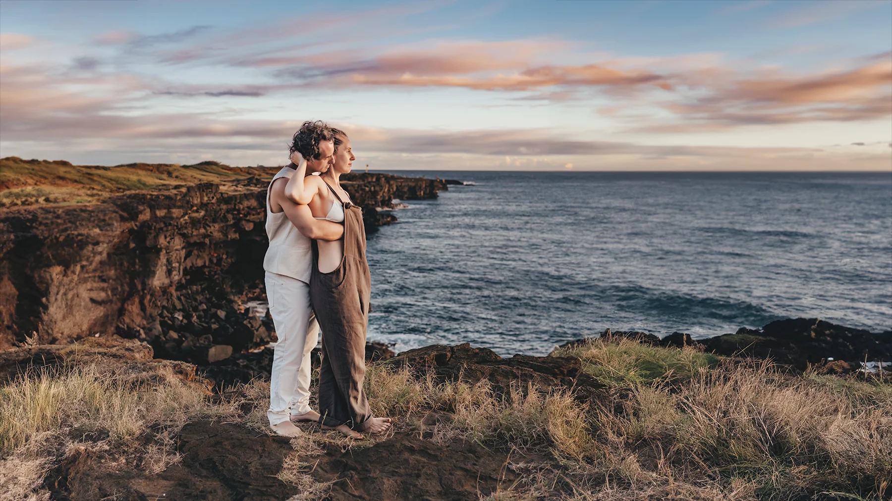 A husband and wife couple standing on a cliff at sunset in Hawaii for their family photoshoot