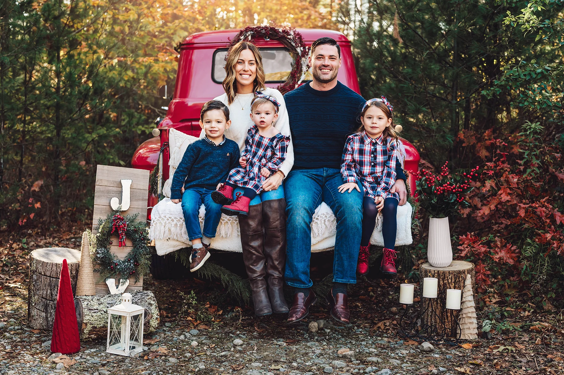 3 kids sitting on an antique red Chevvy Truck decorated for Christmas wearing plaid and denim outfits for their red truck christmas mini session