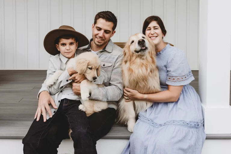 Family being photographed by lyfestyle family photographer Caryn Scanlan. Sitting on their front porch with their 2 golden retrievers.