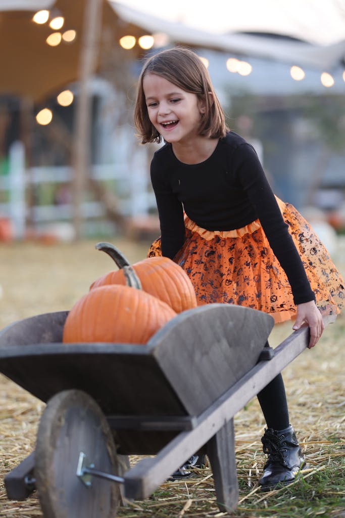 Little Girl Pushing Wooden Wheelbarrow Full of Pumpkins family-friendly fall activities Cape Cod